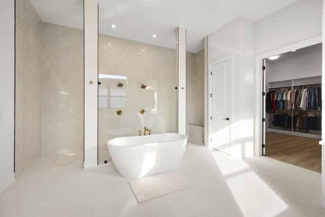 bathroom featuring a freestanding tub, tile walls, a spacious closet, tile patterned floors, and walk in shower