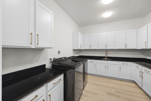 kitchen with washer and clothes dryer, dark countertops, a sink, and white cabinetry