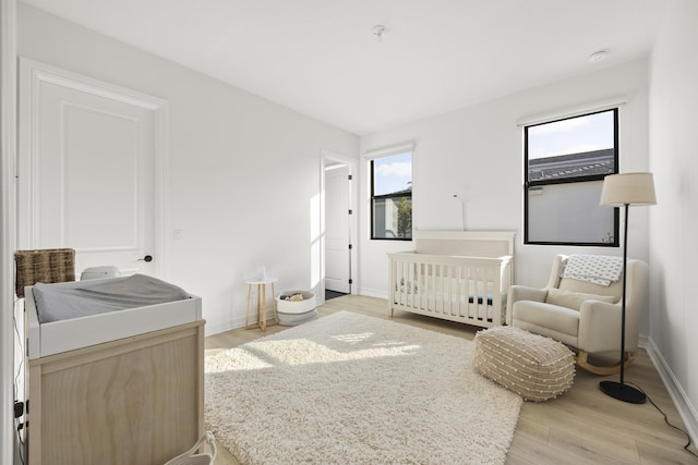 bedroom with light wood-style flooring, baseboards, and a crib