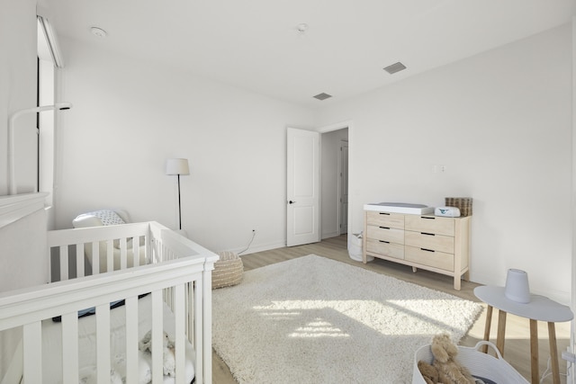 bedroom with visible vents, a crib, light wood-style flooring, and baseboards