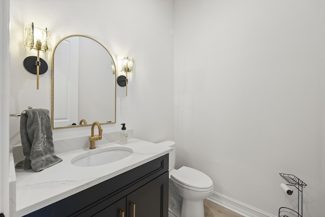 half bath featuring toilet, baseboards, and vanity