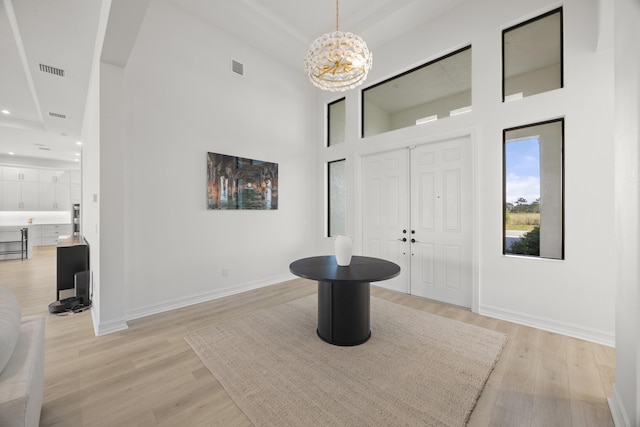 foyer with baseboards, a towering ceiling, visible vents, and light wood-style floors