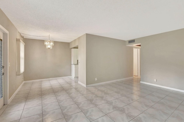 unfurnished room featuring a chandelier, a textured ceiling, and light tile patterned flooring