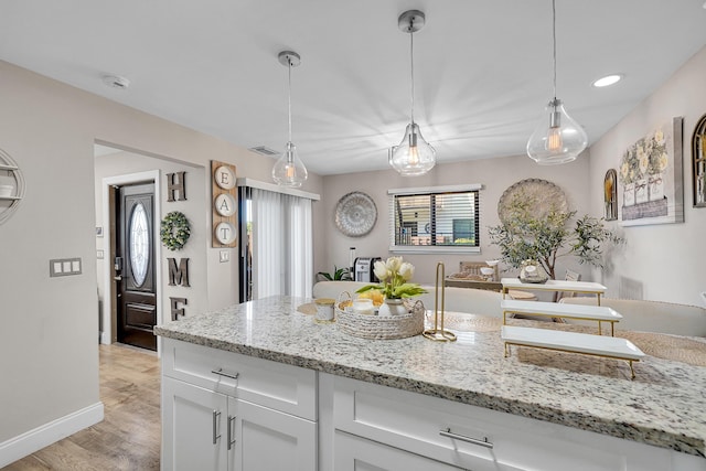 kitchen with white cabinetry, pendant lighting, light stone counters, and light hardwood / wood-style floors