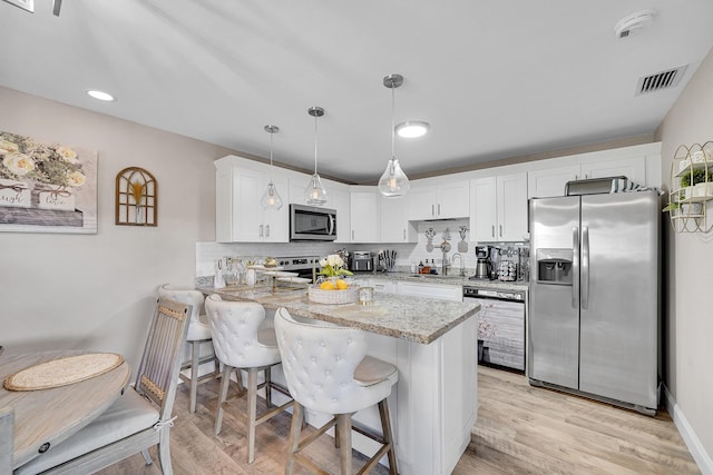 kitchen with appliances with stainless steel finishes, white cabinetry, hanging light fixtures, a kitchen bar, and kitchen peninsula