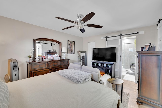 bedroom with a barn door, connected bathroom, ceiling fan, and light hardwood / wood-style flooring