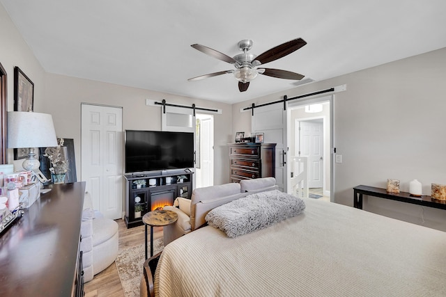 bedroom with a barn door, ceiling fan, and light wood-type flooring