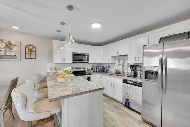 kitchen featuring pendant lighting, appliances with stainless steel finishes, light stone counters, white cabinets, and a kitchen bar