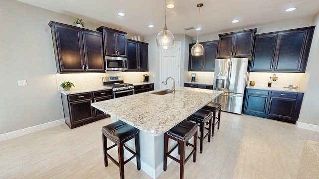 kitchen featuring sink, appliances with stainless steel finishes, a kitchen island with sink, hanging light fixtures, and a kitchen bar