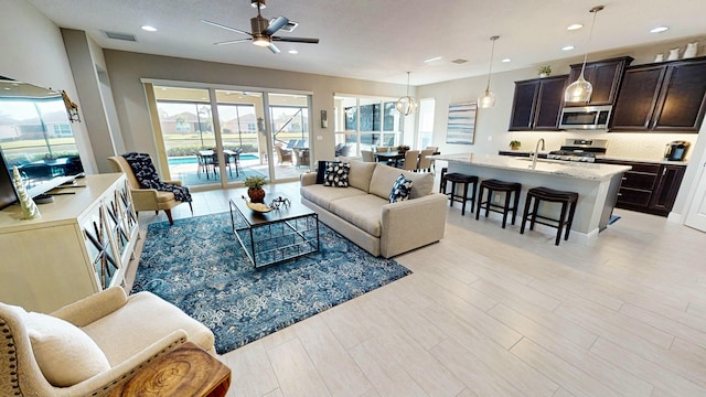 living room featuring sink, light hardwood / wood-style flooring, and ceiling fan