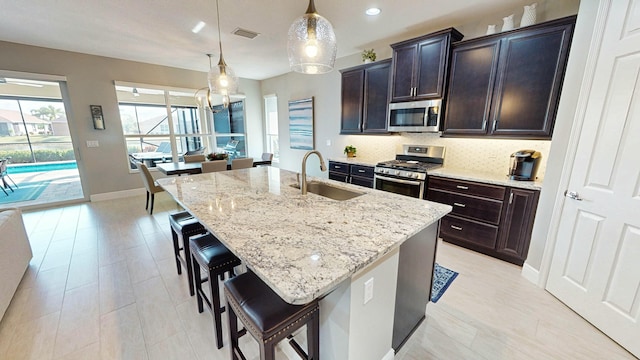 kitchen featuring sink, appliances with stainless steel finishes, hanging light fixtures, a kitchen breakfast bar, and an island with sink