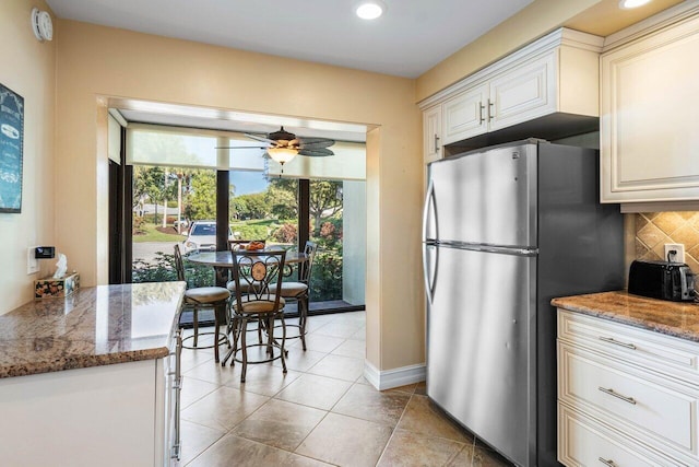 kitchen featuring stone countertops, stainless steel refrigerator, ceiling fan, decorative backsplash, and white cabinets