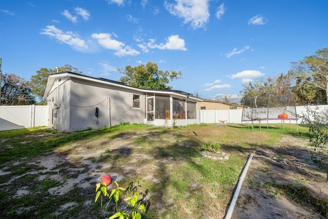 back of house with a trampoline, a lawn, and a sunroom