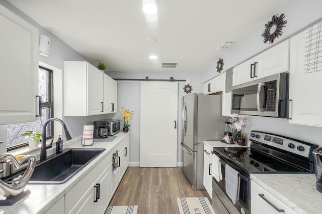 kitchen featuring sink, white cabinetry, stainless steel appliances, a barn door, and hardwood / wood-style floors