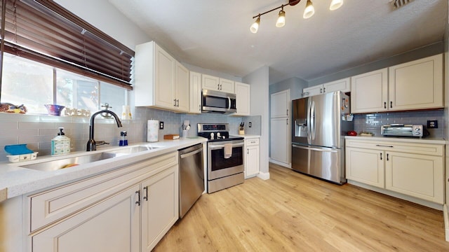 kitchen featuring tasteful backsplash, sink, white cabinets, stainless steel appliances, and light wood-type flooring