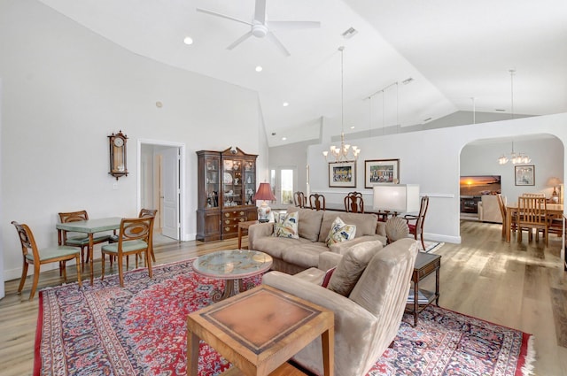 living room with ceiling fan with notable chandelier, high vaulted ceiling, and light wood-type flooring