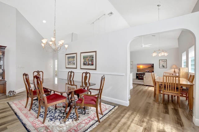 dining area featuring high vaulted ceiling, wood-type flooring, and ceiling fan with notable chandelier