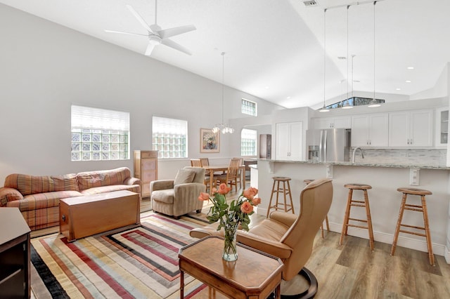 living room with high vaulted ceiling, sink, ceiling fan with notable chandelier, and light wood-type flooring