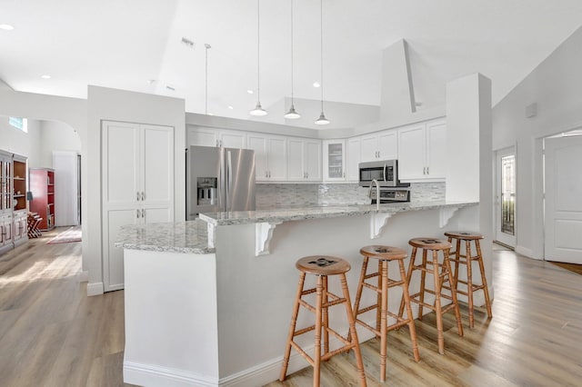 kitchen with appliances with stainless steel finishes, white cabinets, hanging light fixtures, kitchen peninsula, and light stone countertops