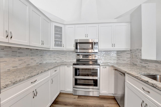 kitchen featuring appliances with stainless steel finishes, dark hardwood / wood-style floors, white cabinetry, decorative backsplash, and light stone countertops