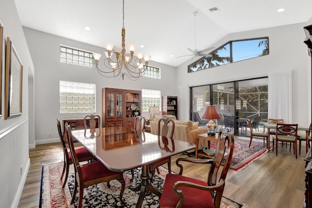 dining space featuring ceiling fan with notable chandelier, wood-type flooring, and high vaulted ceiling