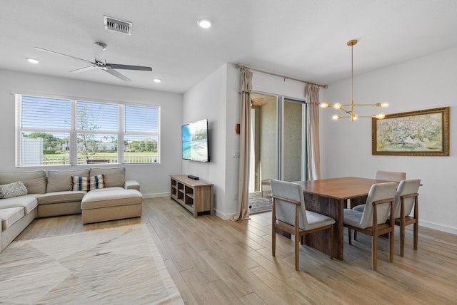 dining space with ceiling fan with notable chandelier and light wood-type flooring