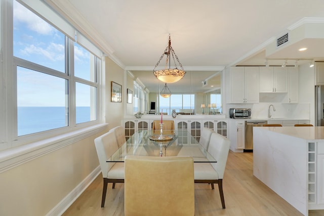 dining area with a water view, crown molding, and light hardwood / wood-style floors