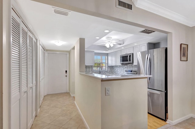 kitchen featuring tasteful backsplash, kitchen peninsula, ceiling fan, stainless steel appliances, and white cabinets