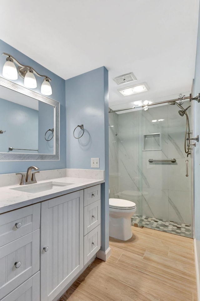 bathroom with hardwood / wood-style floors, vanity, toilet, and a shower with shower door