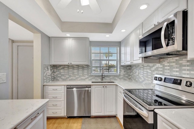 kitchen featuring appliances with stainless steel finishes, a raised ceiling, sink, and white cabinets