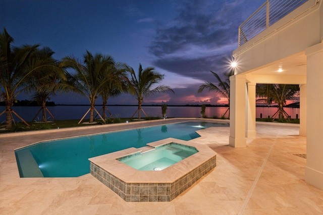 pool at dusk with an in ground hot tub and a patio area