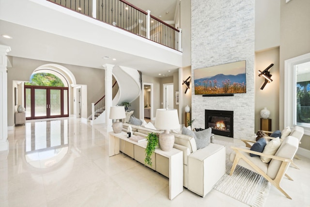 living room featuring decorative columns, a stone fireplace, and a towering ceiling