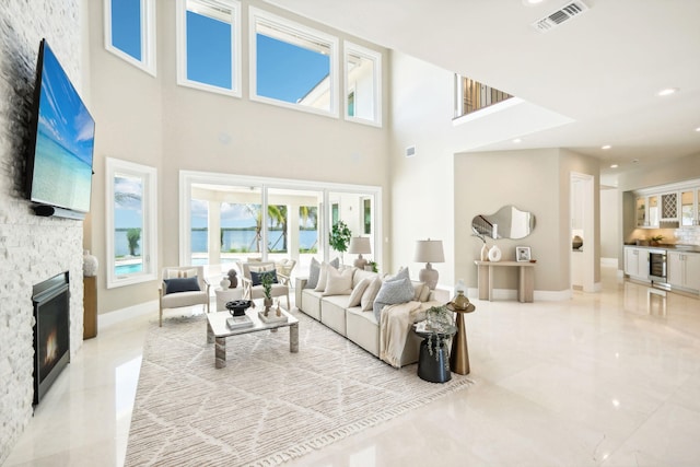 living room featuring beverage cooler, a stone fireplace, and a high ceiling