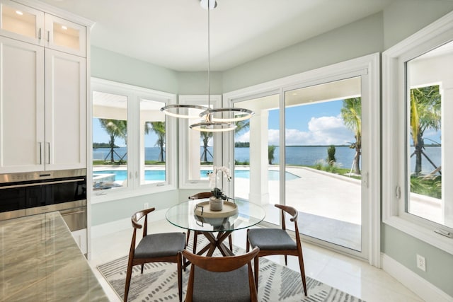 tiled dining room with a water view, a healthy amount of sunlight, and a notable chandelier