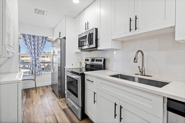 kitchen featuring sink, appliances with stainless steel finishes, white cabinetry, decorative backsplash, and light wood-type flooring