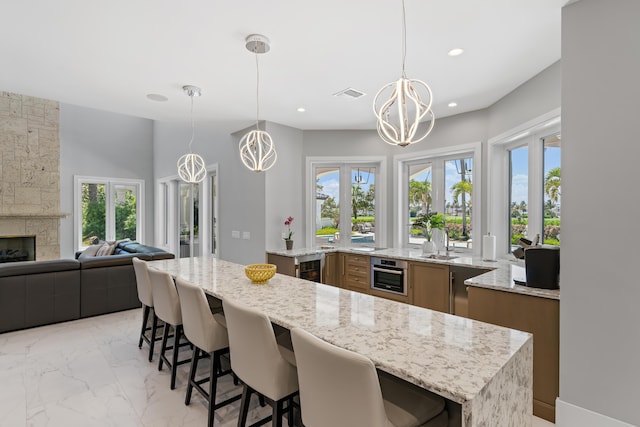 kitchen with hanging light fixtures, light stone countertops, a fireplace, and a kitchen bar