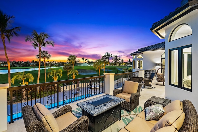 patio terrace at dusk featuring a water view, a balcony, and an outdoor living space with a fire pit