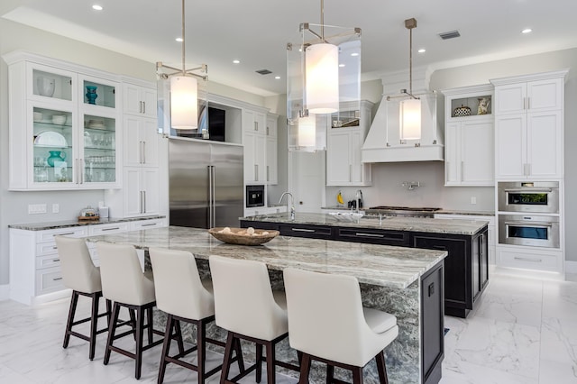 kitchen featuring appliances with stainless steel finishes, decorative light fixtures, a breakfast bar area, a large island with sink, and custom range hood