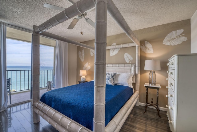 bedroom with floor to ceiling windows, a water view, a textured ceiling, dark hardwood / wood-style flooring, and access to outside