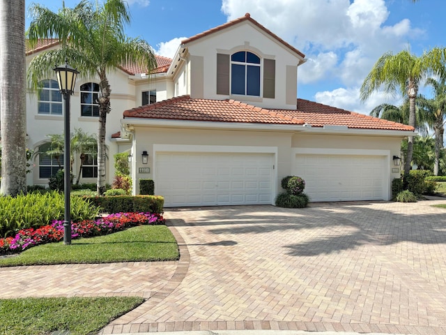 mediterranean / spanish-style house with a garage, decorative driveway, a tile roof, and stucco siding