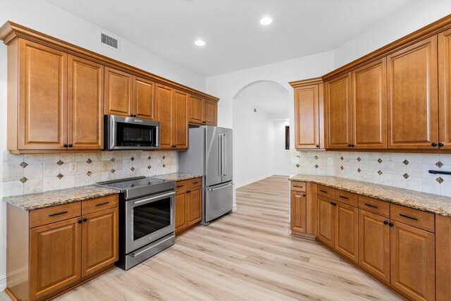 kitchen with brown cabinetry, a sink, stainless steel dishwasher, and light stone countertops