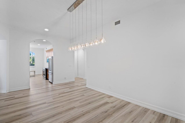 empty room with light wood finished floors, baseboards, visible vents, arched walkways, and recessed lighting