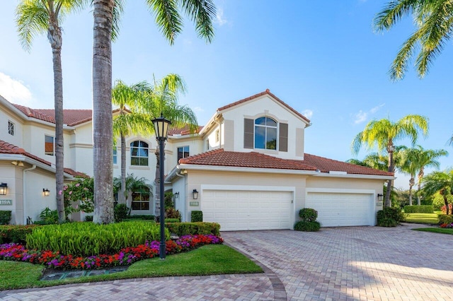 mediterranean / spanish-style house featuring a garage, decorative driveway, a tile roof, and stucco siding