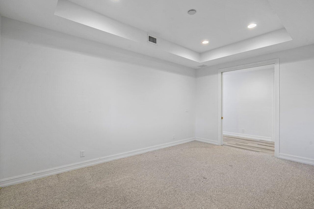 spare room featuring visible vents, baseboards, light colored carpet, a tray ceiling, and recessed lighting