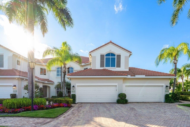 mediterranean / spanish-style house with a garage, decorative driveway, a tile roof, and stucco siding