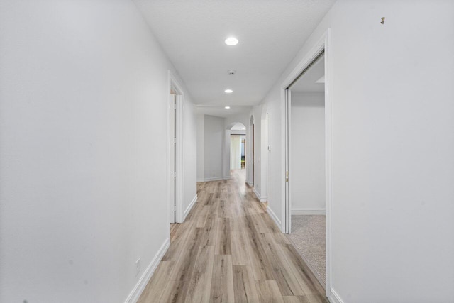 hallway featuring arched walkways, light wood finished floors, baseboards, and recessed lighting