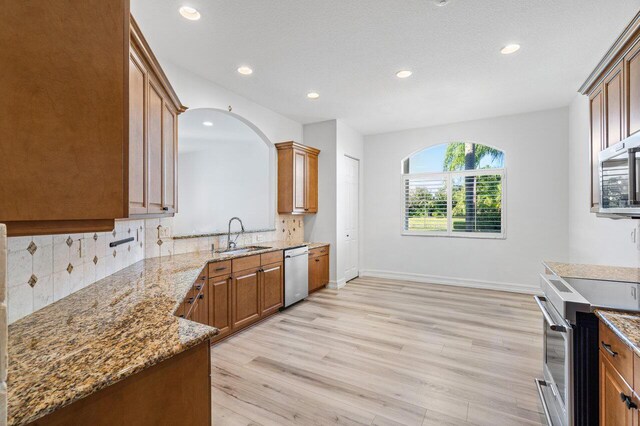 kitchen featuring appliances with stainless steel finishes, backsplash, light stone counters, and light hardwood / wood-style floors