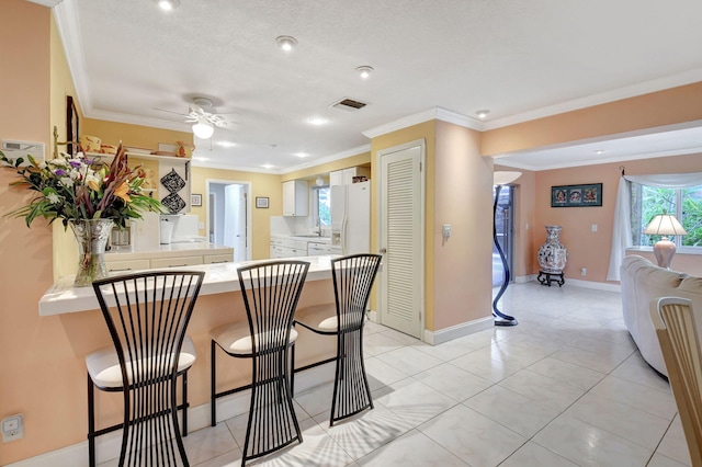 kitchen featuring crown molding, white refrigerator with ice dispenser, white cabinets, a kitchen bar, and kitchen peninsula