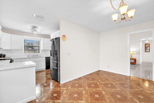 kitchen with a sink, black dishwasher, freestanding refrigerator, tile countertops, and white cabinets