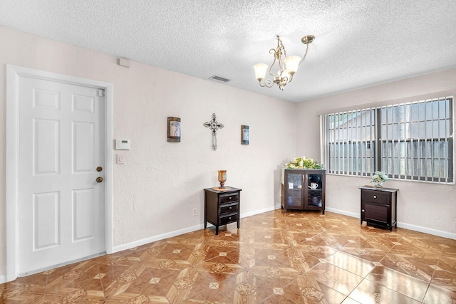 entryway with visible vents, baseboards, an inviting chandelier, a textured wall, and a textured ceiling